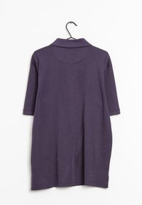 Fioletowa koszulka polo z krótkim rękawem i kołnierzykiem, o gładkiej fakturze i prostym wzornictwie. Wisząca na czarnym wieszaku na jasnym tle.