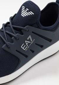 Navy Sneaker aus Mesh mit markanten Schwarz- und Weißdetails. Verfügt über eine Gummisohle und eine kontrastierende Logo-Plakette an der Seite. Schnürdesign.