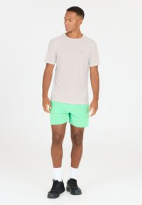 Lys grå kortærmet træningsshirt med et diskret logo, parret med lysegrønne shorts, sorte træningssko og hvide sokker.