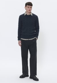 Maglione navy a trecce con una camicia a righe sotto il colletto, abbinato a pantaloni neri dritti e stivali neri stringati.