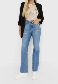 Jeans a vita alta blu chiaro con dettagli strappati, abbinati a una maglietta con motivo marmorizzato e a un blazer nero, completati con sneakers bianche.
