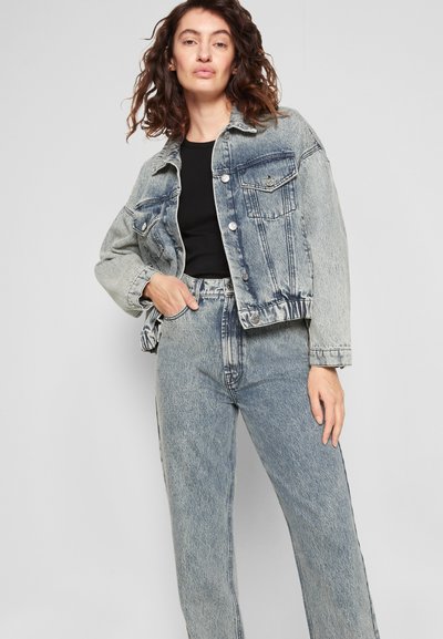 Casaco de ganga azul desbotado com um corte ligeiramente oversized, frente de botões e dois bolsos no peito, combinado com jeans de cintura alta correspondentes.