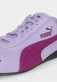 Ανοιχτό μωβ αθλητικό Puma με σκοτεινό ροζ σουέντ ρίγα, καφέ λογότυπο Puma και ταιριαστά ανοιχτό μωβ κορδόνια σε μαύρη σόλα.