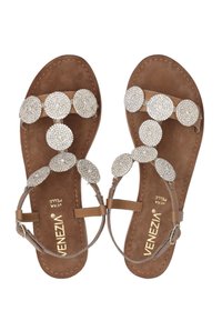 Tanfarbene Sandalen haben eine Reihe von kreisförmigen, geschmückten Akzenten. Die Fußsohle besteht aus einem weichen Material, während die Riemen minimalistisch und schlank sind.
