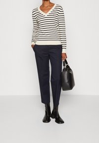 Pull à col en V rayé beige et bleu marine, pantalon bleu marine, bottines noires et sac à main noir. Design épuré avec rayures horizontales et texture lisse.