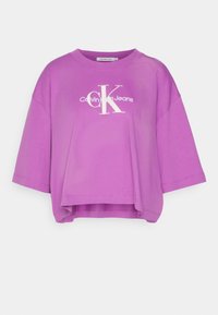 Camiseta corta de manga corta morada, hecha de algodón, que presenta un logo blanco de Calvin Klein y un ajuste holgado con un escote redondeado.