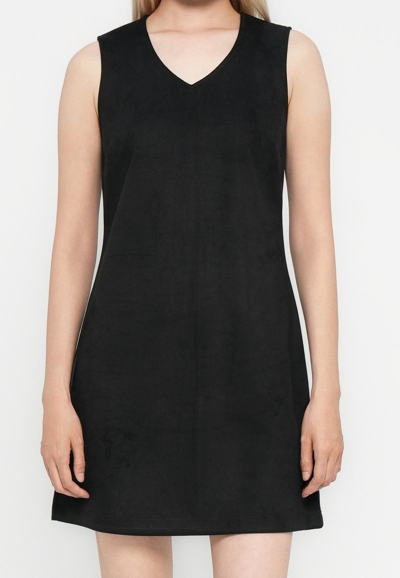 Robe noire sans manches à col en V portée par une personne visible des épaules jusqu'à mi-cuisse sur un fond blanc uni.