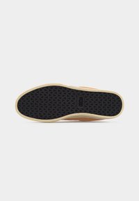 Semelle de chaussure avec motif de grip triangulaire noir, bordure beige et logo "etnies" au centre, sur un fond gris clair uni.