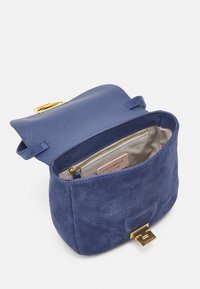 Blå mocka- och läderhandväska med guldfärgat spänne, öppen för att visa beige foder och innerficka med dragkedja och varumärkesetikett.