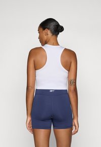 Top sportiv alb cu design racerback, asociat cu pantaloni scurți ajustați de culoare albastru marin. Textură netedă, marcaj minim pe talie.