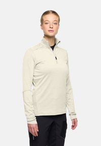 Licht beige kwart-zip pullover van gladde, vochtregulerende stof. Heeft lange mouwen en een kleine rits bij de kraag.