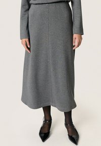 Gonna midi grigia realizzata in un materiale morbido con una leggera lucentezza. Presenta una forma dritta, una texture liscia e un orlo semplice. Indossata con scarpe nere a punta.