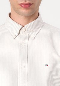 Camisa de cuadros en crema claro y beige, con un cuello clásico y un pequeño logotipo bordado en el pecho.