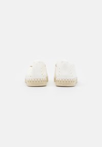 Zapatillas de goma blancas con diseño perforado, suela beige y costuras de acento. Textura suave con punta redonda y bucle en la parte trasera para facilitar su uso.
