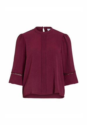 Bordos spalvos palaidinė su pynimo detalėmis priekyje, 3/4 pūsti rankoviai su blizgučių apdaila ir aukštu apvaliu kaklu su užsegimu atgal.