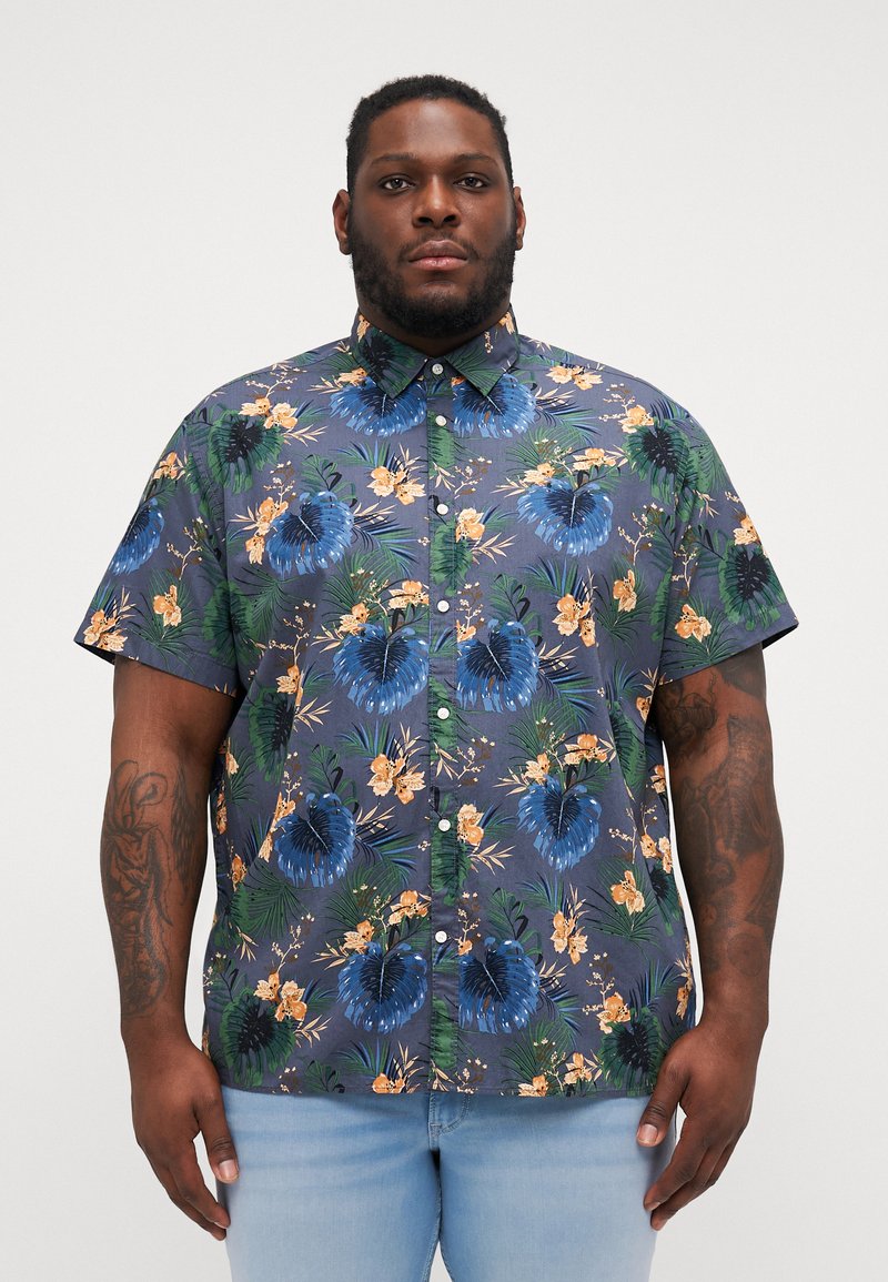 Camisa de botones de manga corta en azul oscuro con un patrón floral tropical en verde, azul y naranja. Tejido suave con un corte relajado.