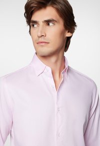 Jasnoróżowa koszula z guzikami, wykonana z jednolitego, teksturowanego materiału, z klasycznym kołnierzykiem i subtelnym detalem w postaci przeszyć przy guzikach.