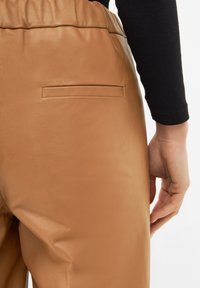 Tan leather pants with a smooth texture, featuring a small rear pocket. The waistband is gathered for a relaxed fit.