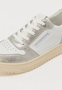 Sneaker bianco con accenti metallico argento, in pelle testurizzata e materiali sintetici, caratterizzata da dettaglio perforato sulla punta e patch con logo sul lato.