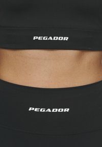 Zwarte sportieve cropped top en hoge taille legging met het 'PEGADOR' logo in het wit. Glad, rekbaar materiaal, naadloos ontwerp, minimalistische stijl.