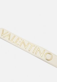 Valentino-logoband i krämfärgad läder med embossat guldtryck. Har en slät, mjuk textur och rena kanter.