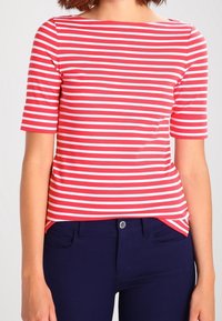 Červenobíle pruhovaný krátký rukáv top s lodičkovým výstřihem, přiléhavým střihem a měkkou tkaninou. Vyznačuje se modrými kalhotami s předními kapsami.
