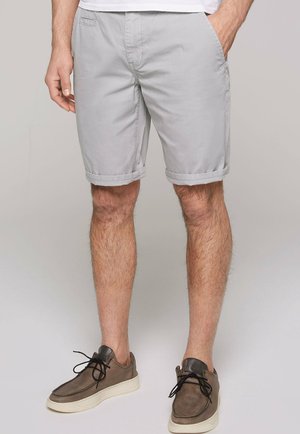 Shorts gris clair en mélange de coton, avec une coupe décontractée, des poches latérales et des ourlets retroussés. Associés à des chaussures décontractées sombres.