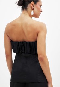 Czarny top bez ramiączek z falbaniastym akcentem z tyłu, charakteryzujący się gładką fakturą i dopasowanym krojem.