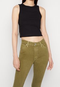Musta ribbed crop-top, jossa on pyöreä pääntie, yhdistettynä korkeavyötäröisiin oliivinvihreisiin farkkuihin, joissa on etutaskut ja kontrastivärinen ommel.