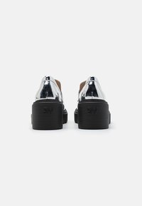 Sølvmetallic platform sko med en blank overflade, sorte rillet såler og minimalistisk design. Har et præget logo på hælen.