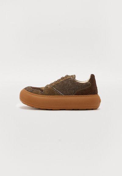 Brązowy zamszowy sneaker z puszystą fakturą i gumową podeszwą. Posiada wyściełany kołnierz i zaokrąglony nosek. Wiązany na okrągłe przelotki z przodu.