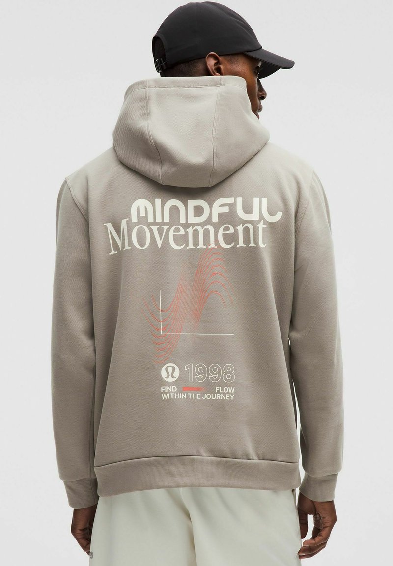 Felpa grigia con una grande stampa bianca del testo "MINDFUL Movement" sul retro, caratterizzata da grafiche di onde rosse e l'anno "1998" in basso.