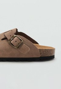 Brun mockasinsandal med justerbar metallspänne, korkfotbädd och svart gummisula. Öppnat design med utskärningar för andningsförmåga.