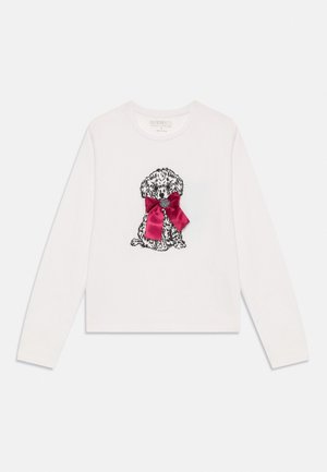 Vit långärmad skjorta med svart broderad valp som bär en stor röd satinrosett runt halsen, placerad centralt fram.