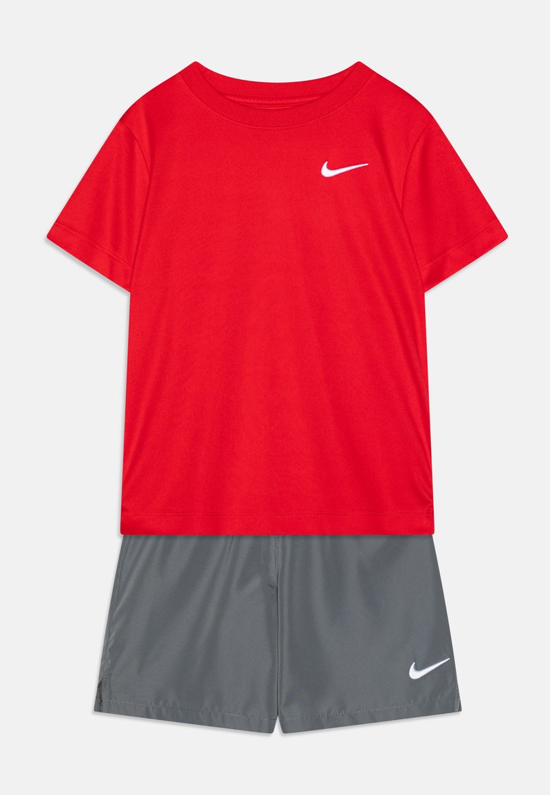 Κόκκινο κοντομάνικο T-shirt με λευκό λογότυπο Nike στο στήθος, συνδυασμένο με γκρι σορτς που διαθέτει μικρό λευκό λογότυπο Nike. Και τα δύο είναι φτιαγμένα από ελαφρύ υλικό.