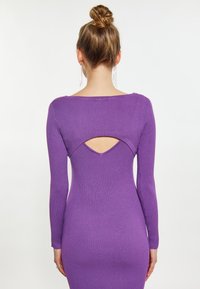 Langärmliges, geripptes Kleid in Lila mit einem Ausschnitt auf dem Rücken. Glatte Textur und taillierte Passform, die die Figur betont.