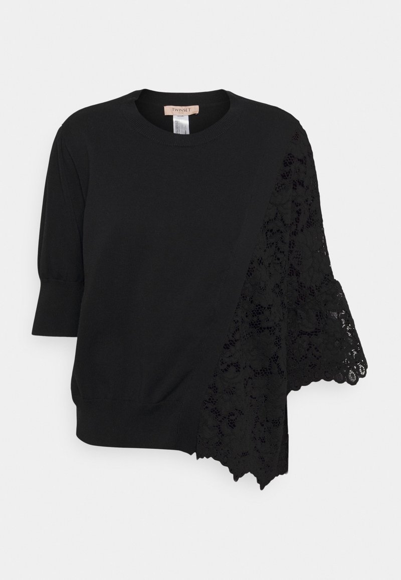 Haut noir en maille à manches courtes avec encolure ronde et panneau asymétrique en dentelle florale s'étendant de l'épaule jusqu'à un côté.