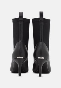 Ett par svarta högklackade ankelstövlar med smala klackar, slät läderbaksidan, sträckbart tyg på skaftet och Calvin Klein-logotyp på klackfliken.
