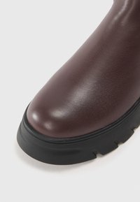 Bottine en cuir marron à bout rond, surface texturée et semelle en caoutchouc noir épais avec des rainures pour l'adhérence.
