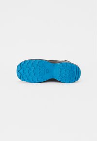 Semelle de chaussure de sport noire avec un motif de crampons bleu prononcé. La semelle présente des grips texturés et un motif multi-directionnel pour une adhérence optimale.