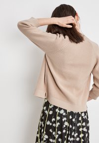 Světle béžový pletený svetr s třičtvrtinovými rukávy, představující strukturované žebrování a lehce rozšířený, zkrácený střih.