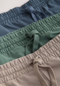 Tres pares de pantalones con cintura elástica en azul, verde y beige, cada uno con un nudo de cordón atado en la parte delantera.