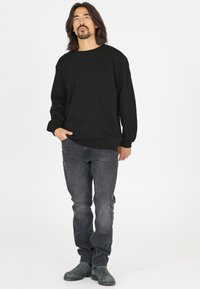 Musta collegepaita, jossa on pyöreä kaula-aukko, ribbireunukset ja laskeutuvat olkapäät, yhdistettynä tummanharmaisiin farkkuihin ja mustiin saappaisiin. Yksinkertainen ja rento muotoilu.