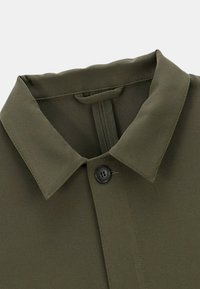 Col de chemise vert olive avec un seul bouton noir fixé en haut, avec une boucle cousue à l'intérieur.