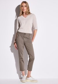 Haut beige clair à col en V avec des manches trois-quarts, associé à un pantalon chino vert olive. Baskets blanches, tissu lisse, coupe ajustée, détails minimalistes.