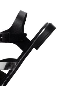 Sandalo in pelle nera con suola piatta, dotato di una fascia metallica argento e un dettaglio con fibbia. Il design è semplice e presenta linee pulite.