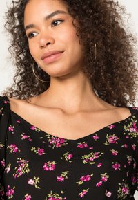 Blusa preta com padrão floral, apresentando um design de decote em V, mangas curtas e pequenos padrões de flores rosas e verdes em um tecido texturizado.