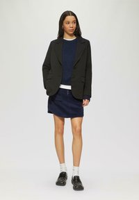 Blazer noir avec deux poches avant, pull en tricot bleu marine, jupe en velours côtelé bleu marine, chaussettes blanches et mocassins décoratifs noirs avec des clous.