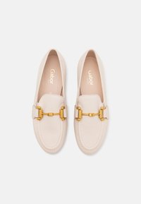 Beige leren loafers met een ronde neus, voorzien van een goudkleurige kettingaccent aan de voorkant. Glad uiterlijk en minimale stikseldetails.