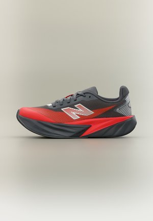Сиви и червени маратонки New Balance с бели лога и дебела черно-червена подметка на светло бежов фон.